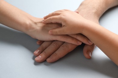 Photo of Parents and child holding hands together on gray background, closeup