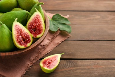 Photo of Cut and whole green figs in bowl on wooden table, closeup. Space for text