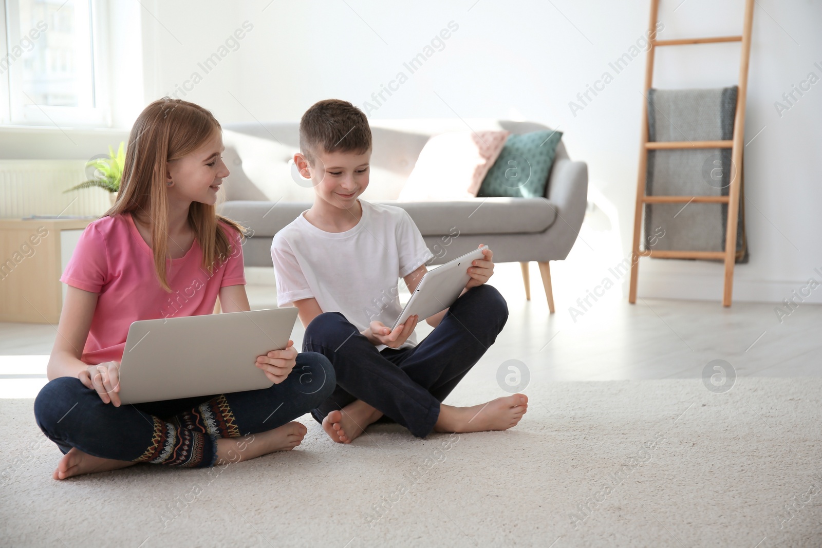 Photo of Teenage girl and her brother with laptop sitting on cozy carpet at home