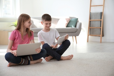 Photo of Teenage girl and her brother with laptop sitting on cozy carpet at home