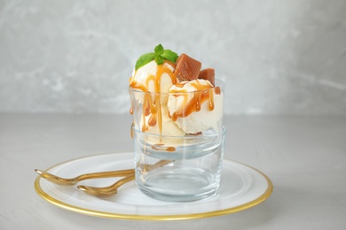 Delicious ice cream with caramel sauce, candies and mint served on light grey table