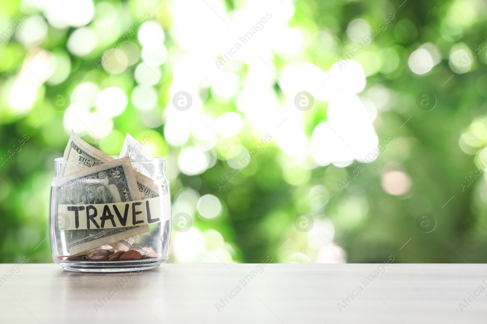 Photo of Glass jar with money and label TRAVEL on table against blurred background. Space for text