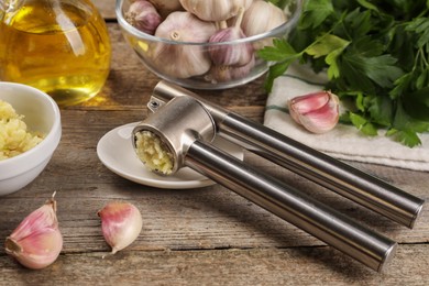 Photo of Garlic press and products on wooden table, closeup