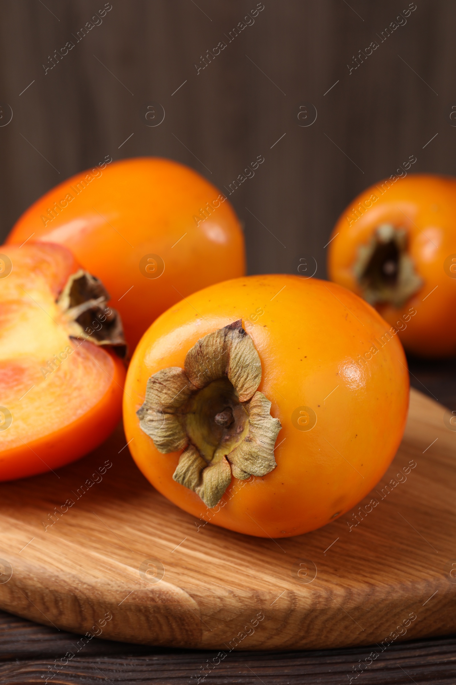 Photo of Whole and cut delicious ripe persimmons on wooden table, closeup