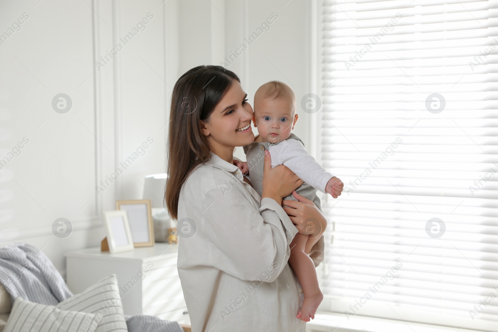 Photo of Young woman with her little baby near window at home