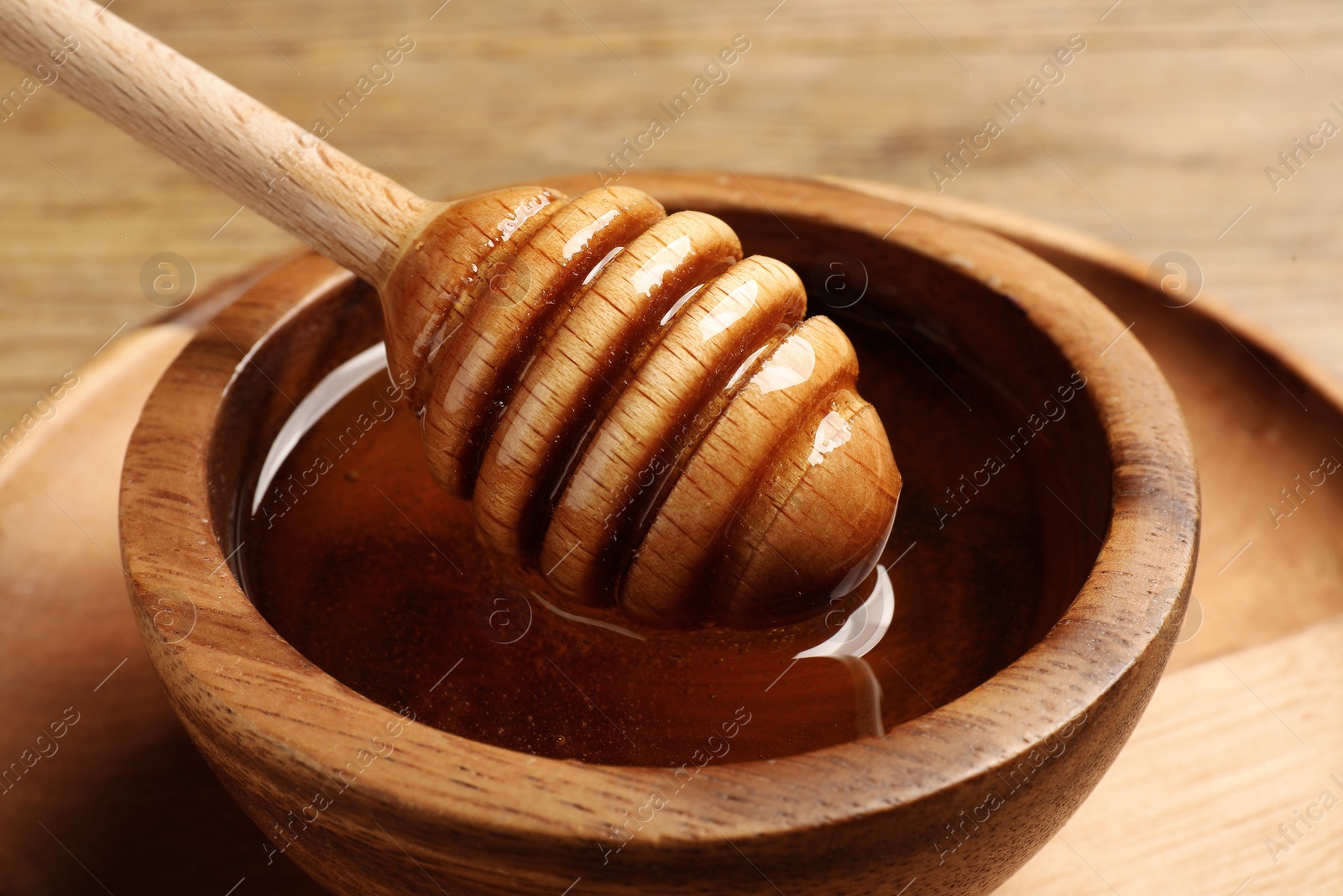 Photo of Dipper with honey in wooden bowl at table, closeup