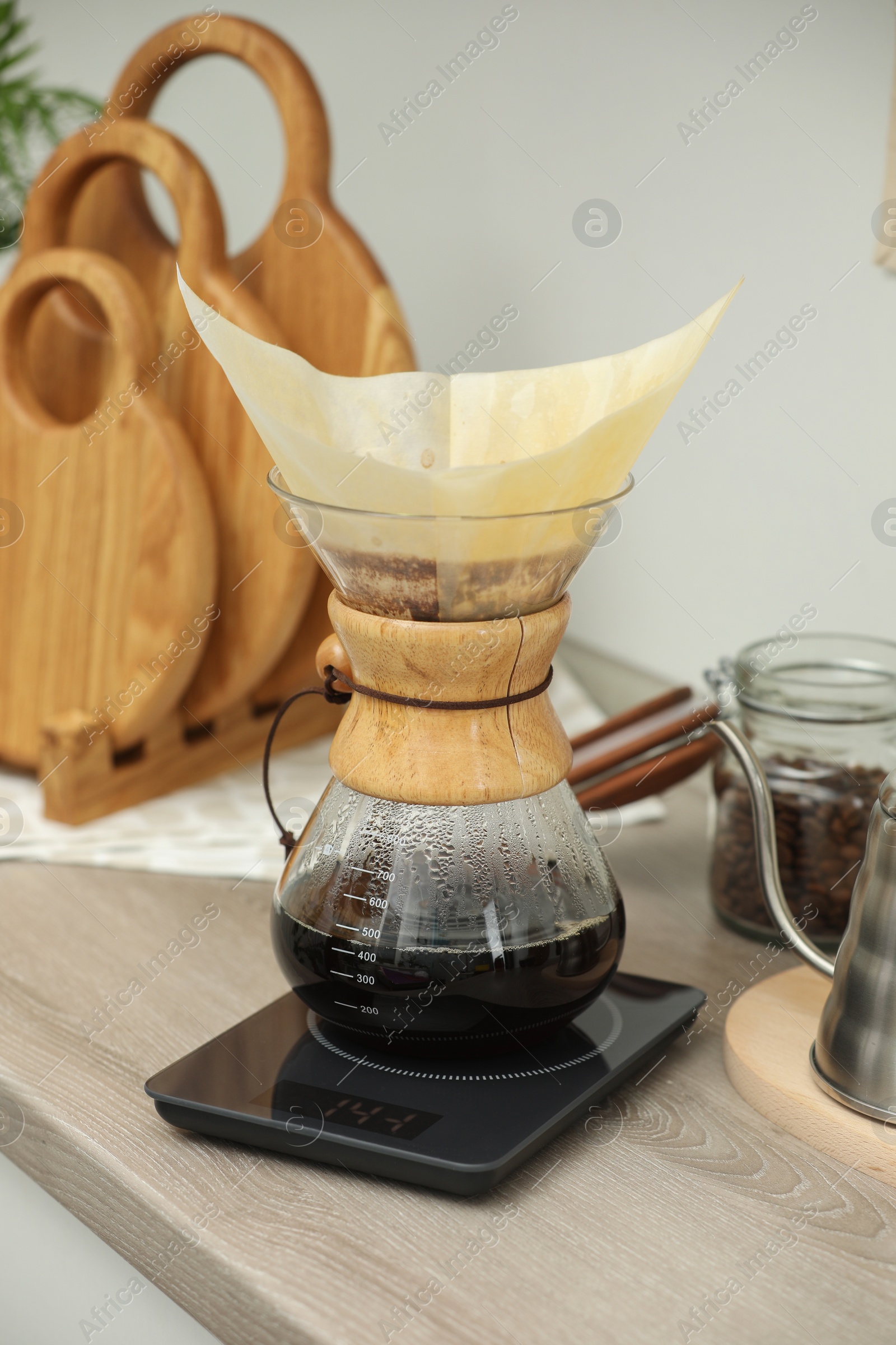 Photo of Glass chemex coffeemaker with paper filter and coffee on wooden countertop in kitchen