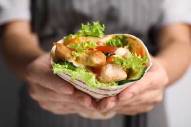 Woman holding delicious shawarma with chicken meat and vegetables, closeup