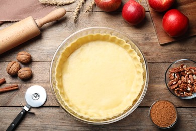 Photo of Flat lay composition with raw dough and ingredients for apple pie on wooden table
