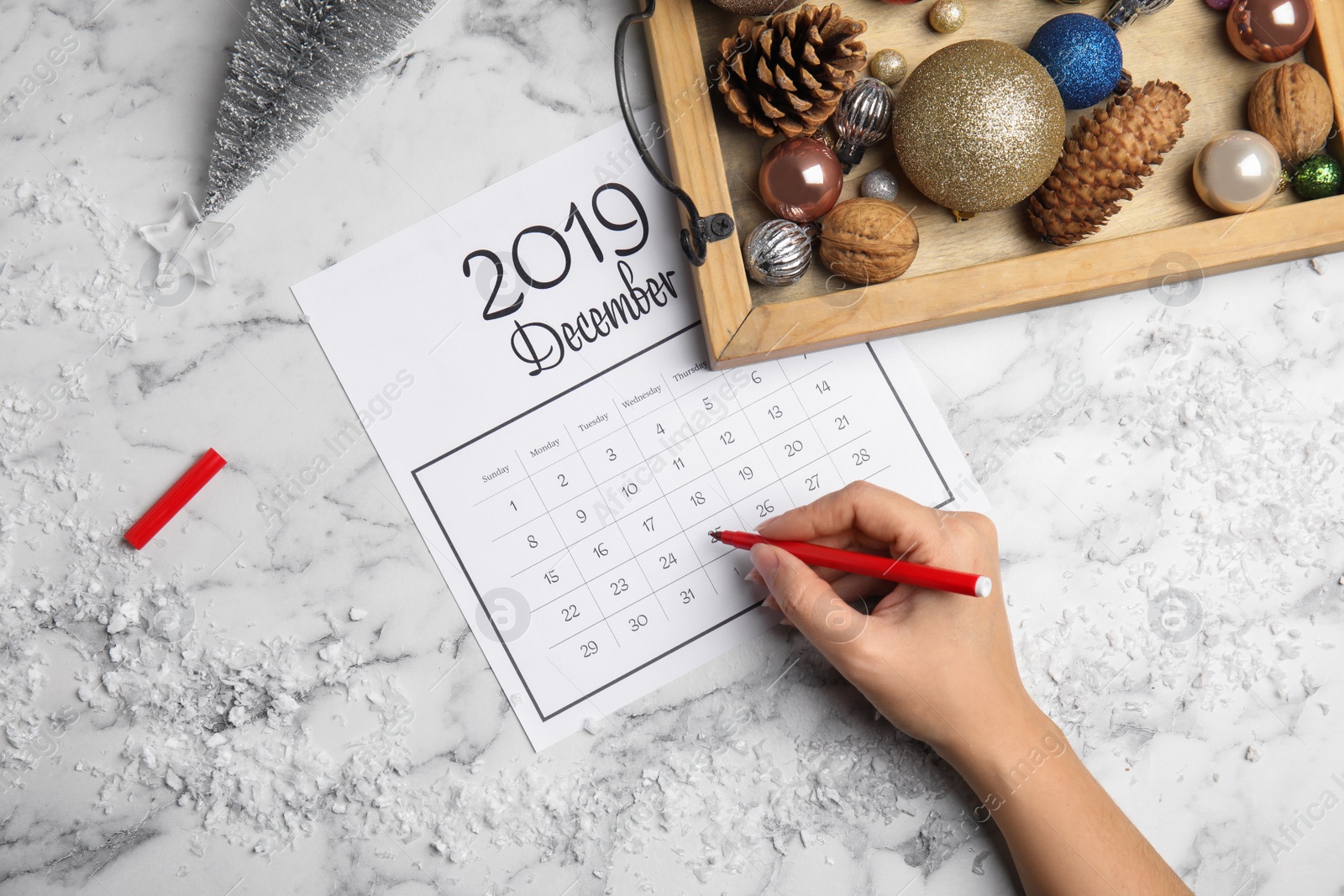 Photo of Woman marking date in calendar at white marble table, top view