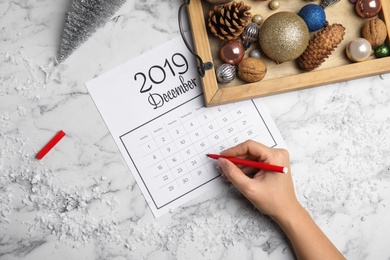 Photo of Woman marking date in calendar at white marble table, top view