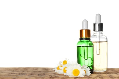 Bottles of chamomile essential oil and flowers on wooden table, white background