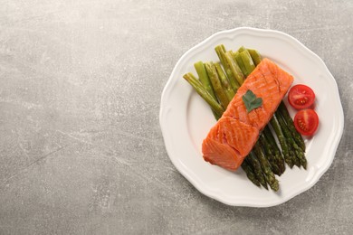 Photo of Tasty grilled salmon with tomatoes and asparagus on grey table, top view. Space for text