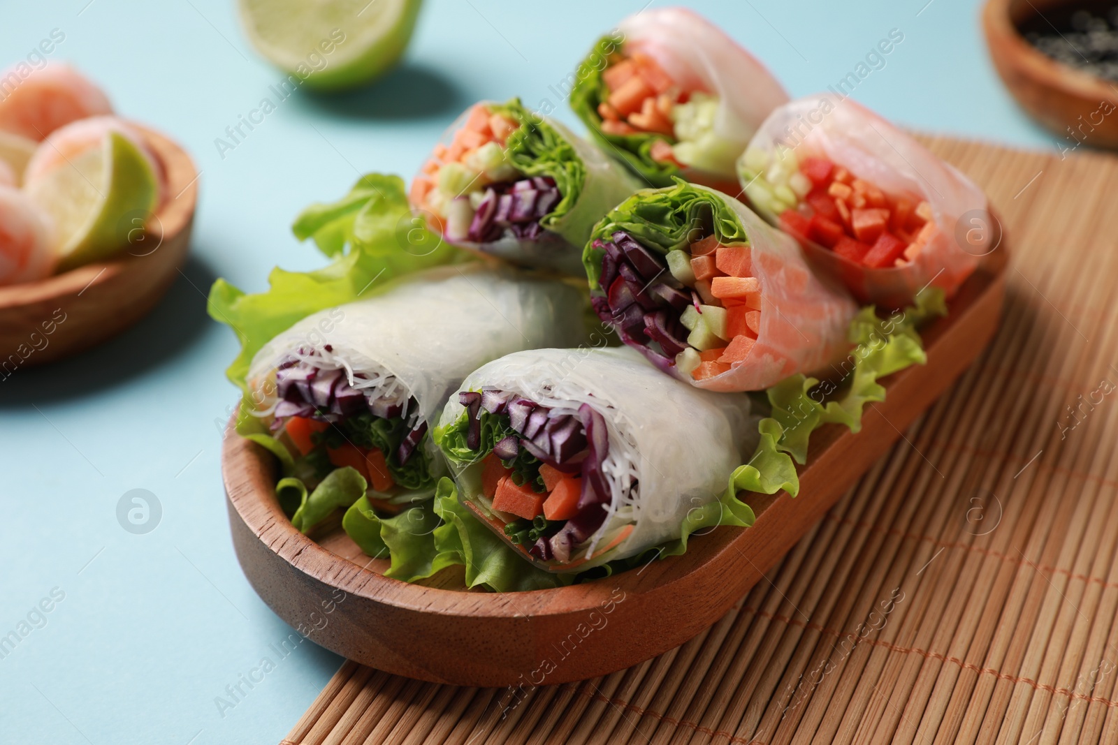 Photo of Tasty spring rolls served with lettuce on light blue background, closeup