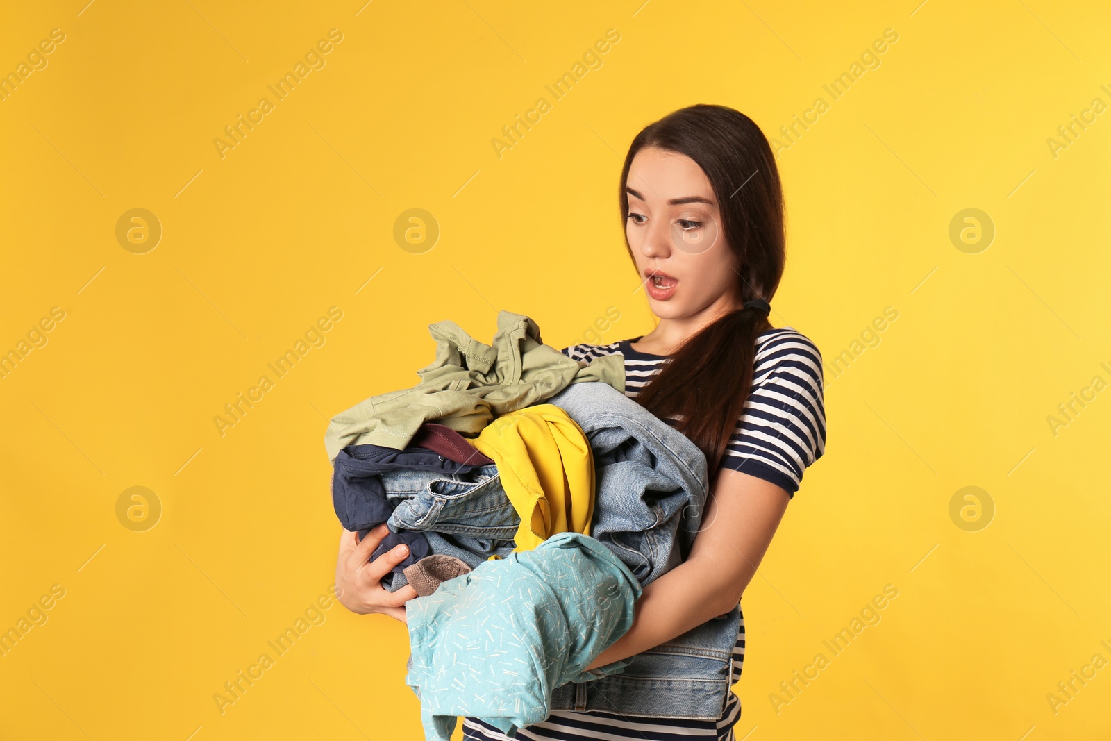 Photo of Emotional young woman holding pile of dirty laundry on color background