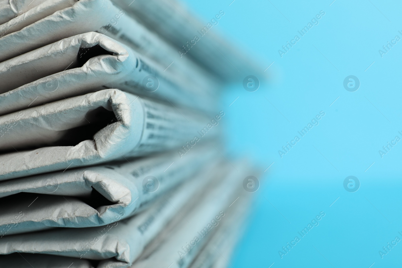 Photo of Stack of newspapers on light blue background, closeup with space for text. Journalist's work