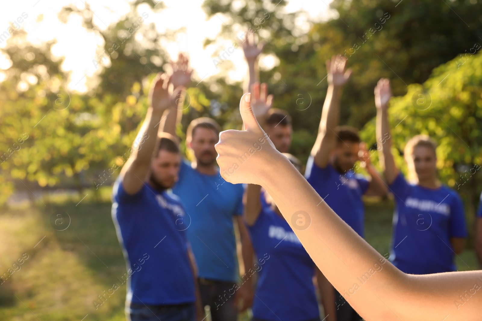 Photo of Woman showing thumb up at volunteers meeting. Group of people outdoors