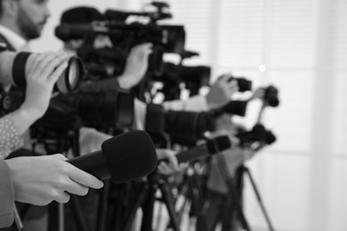 Image of Professional journalists with microphones and cameras indoors, closeup. Black and white effect