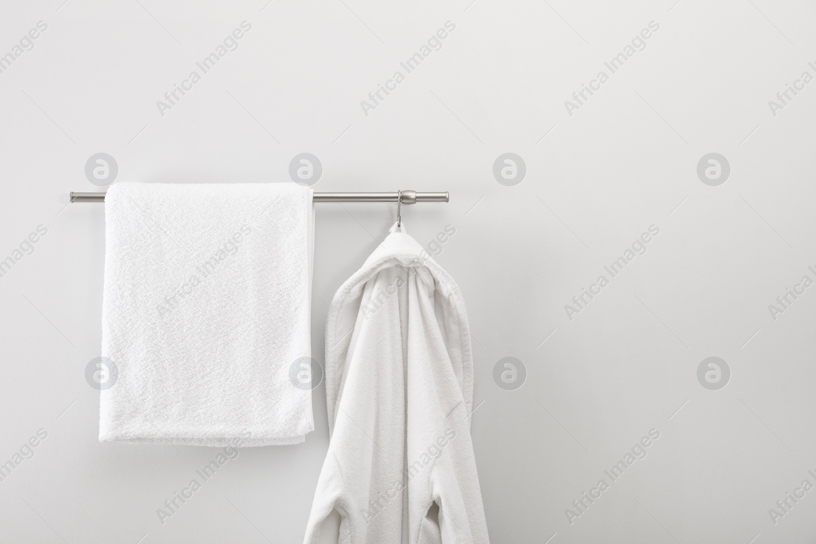 Photo of Rack with clean bathrobe and towel on light wall