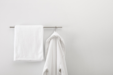 Rack with clean bathrobe and towel on light wall