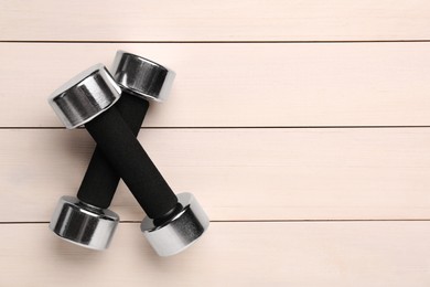 Photo of Metal dumbbells on white wooden table, flat lay. Space for text