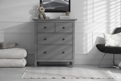 Stylish room interior with grey chest of drawers and comfortable chair
