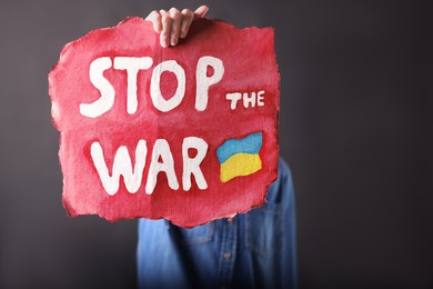 Photo of Woman holding poster with words Stop the War on black background, closeup