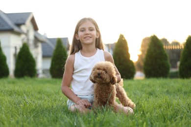 Beautiful girl with cute Maltipoo dog on green lawn in backyard