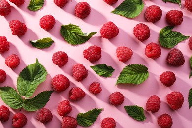 Photo of Tasty ripe raspberries and green leaves on pink background, flat lay