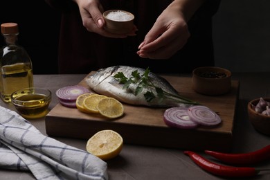 Photo of Woman salting raw dorado fish at grey table, closeup