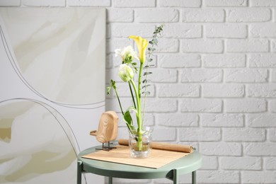 Beautiful ikebana for stylish house decor. Floral composition with fresh flowers and eucalyptus branch on coffee table near white brick wall