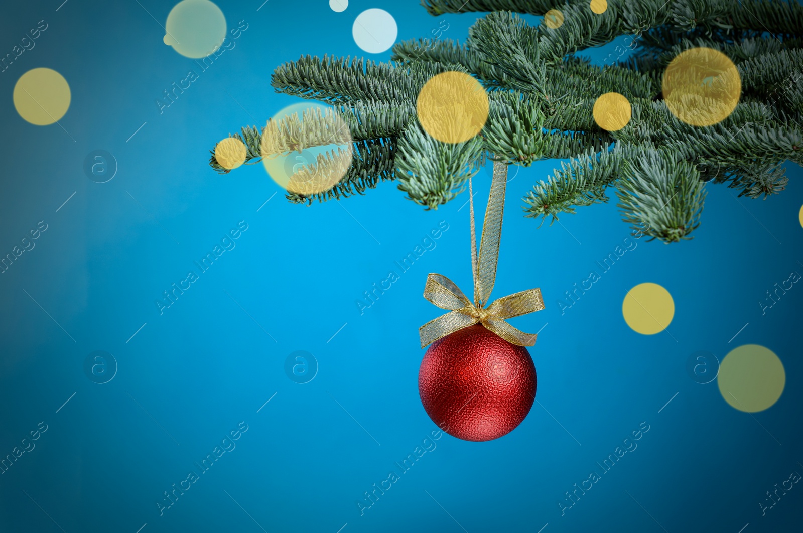 Photo of Beautiful Christmas ball hanging on fir tree branch against light blue background, bokeh effect. Space for text