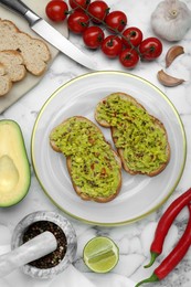 Photo of Delicious sandwiches with guacamole and ingredients on white marble table, flat lay
