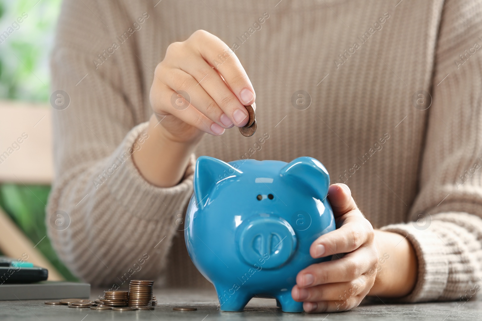 Photo of Woman putting money into piggy bank at table, closeup