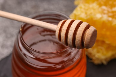 Sweet golden honey in jar and dipper on table, closeup