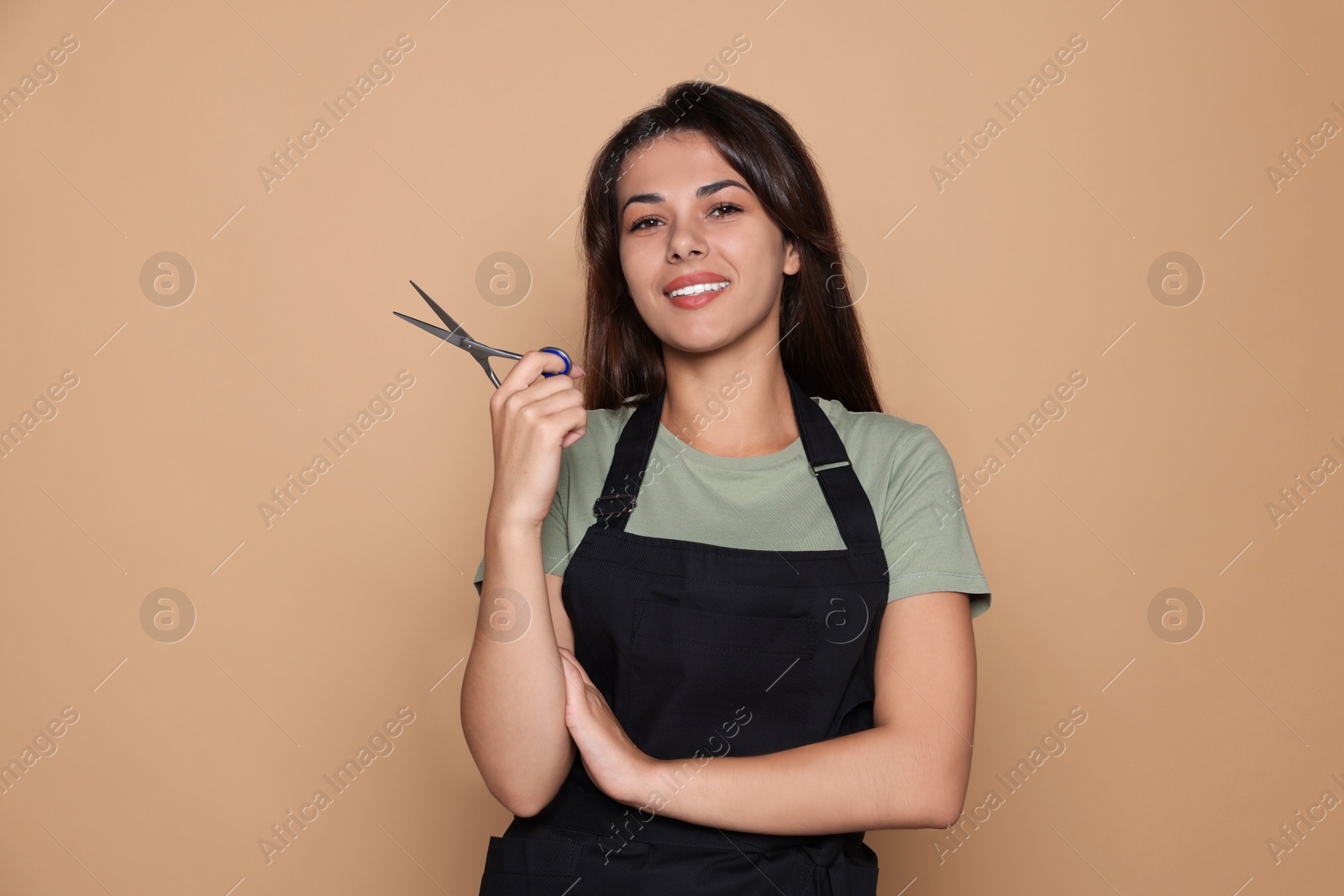 Photo of Portrait of happy hairdresser with professional scissors against pale orange background