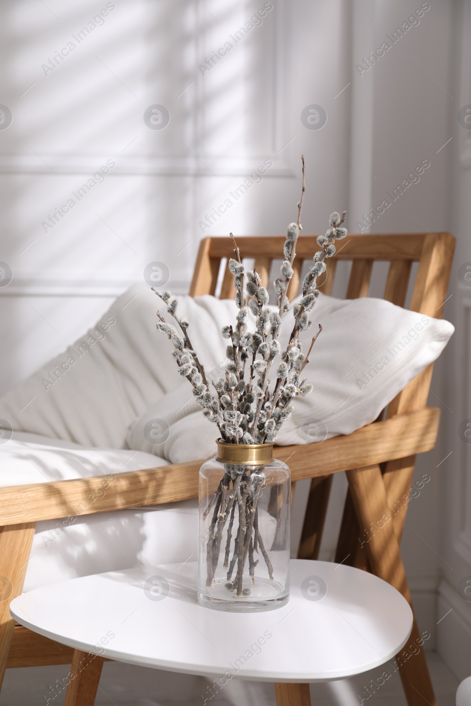 Photo of Glass vase with pussy willow tree branches on table near armchair in room