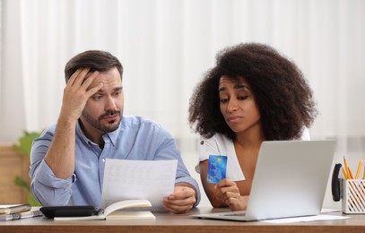 Confused couple with debt notification and credit card planning budget at table indoors. Financial problem