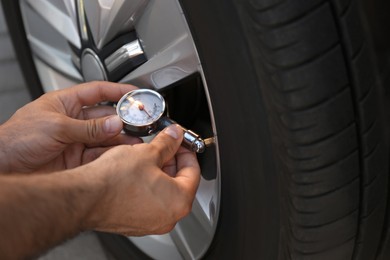 Photo of Man checking air pressure in car tire, closeup
