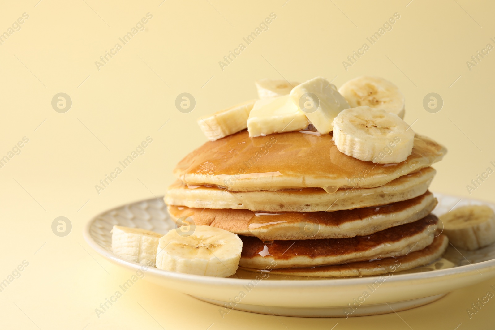 Photo of Delicious pancakes with bananas, honey and butter on beige background, closeup. Space for text