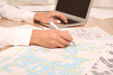 Professional cartographer working with cadastral map at wooden table, closeup