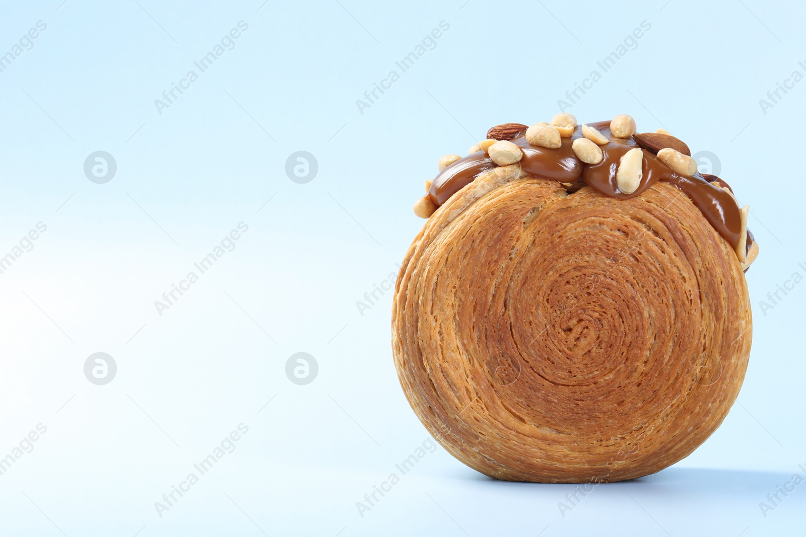 Photo of One supreme croissant with chocolate paste and nuts on light blue background, closeup with space for text. Tasty puff pastry
