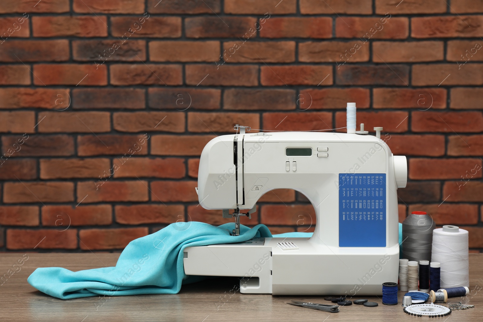 Photo of Sewing machine with fabric and craft accessories on wooden table against brick wall