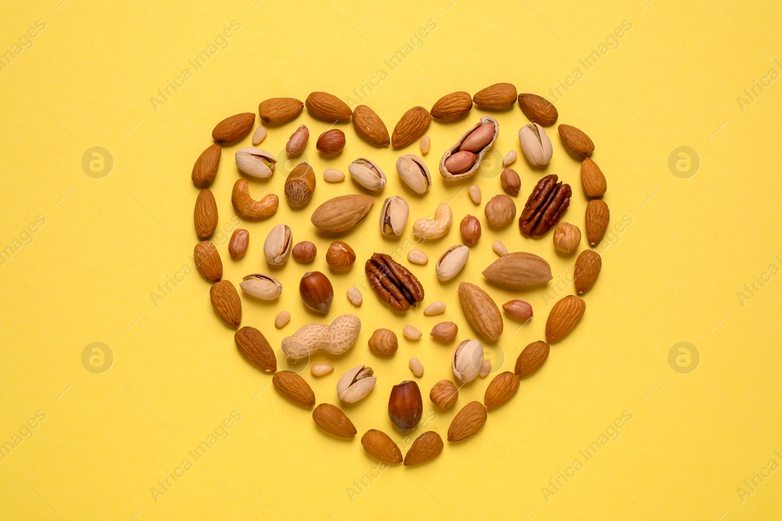 Photo of Heart made of different nuts on yellow background, flat lay