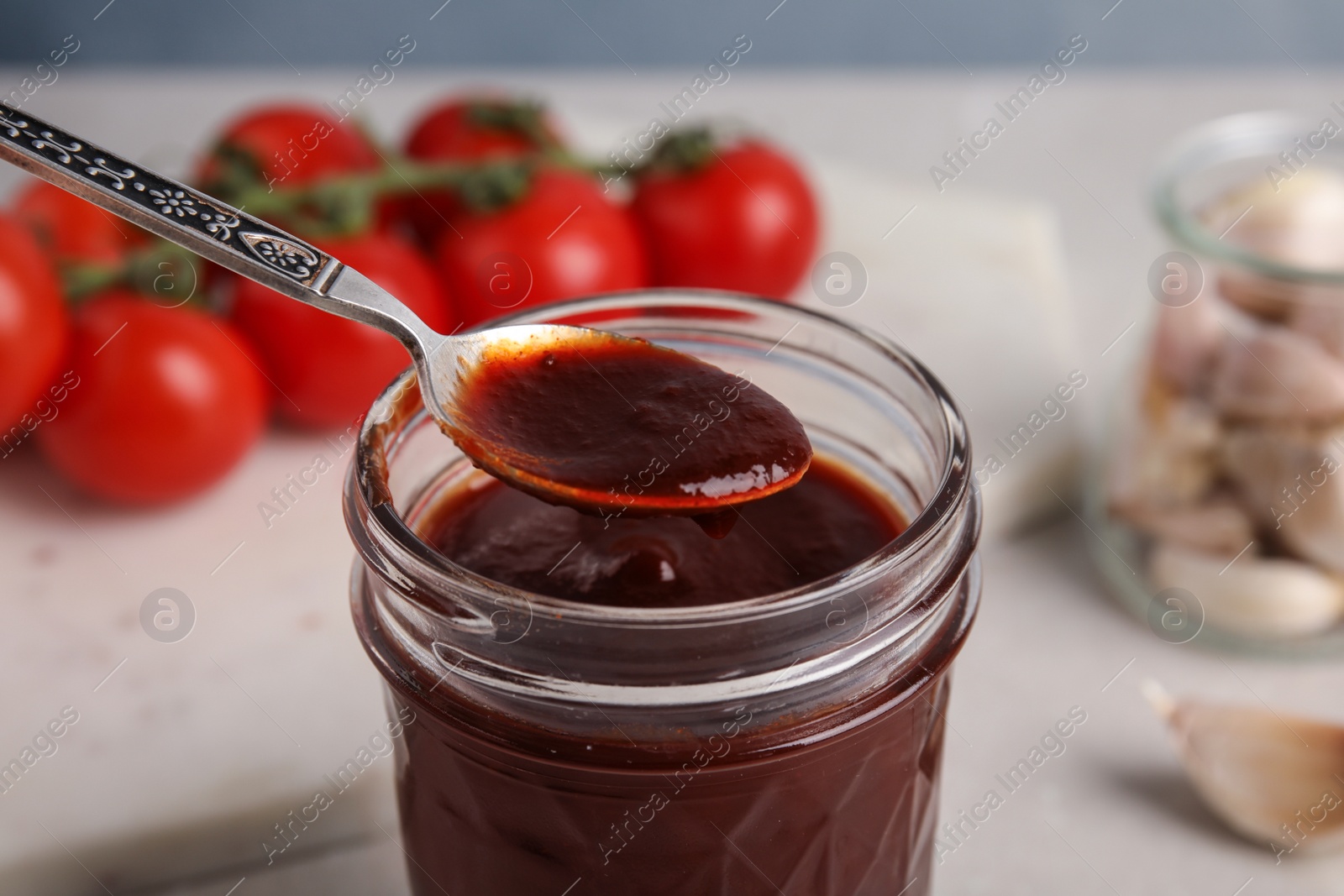 Photo of Jar and spoon with barbecue sauce on table, closeup