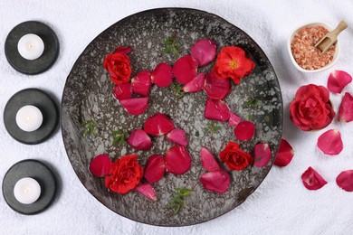Photo of Plate with water, rose petals, burning candles and sea salt on white towel, flat lay. Pedicure procedure