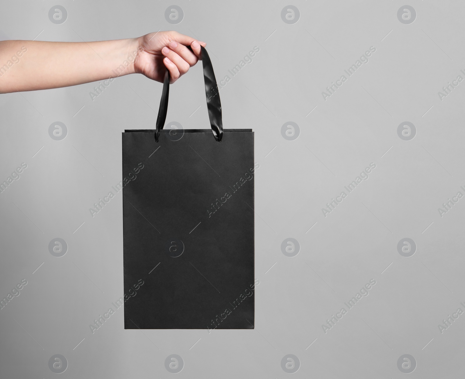 Photo of Woman holding paper shopping bag on grey background, closeup. Space for text