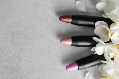 Photo of Set of bright lipsticks and spring flowers on grey background, flat lay. Space for text