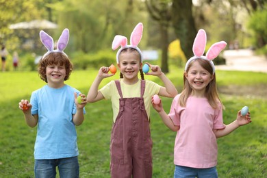 Photo of Easter celebration. Cute little children in bunny ears holding painted eggs outdoors