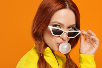 Photo of Portrait of beautiful woman in sunglasses blowing bubble gum on orange background
